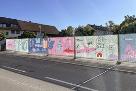 Von Kindern gestaltete Gemälde auf dem Bauzaun, die zeigen, was wichtig für das Zuhause der Kinder ist