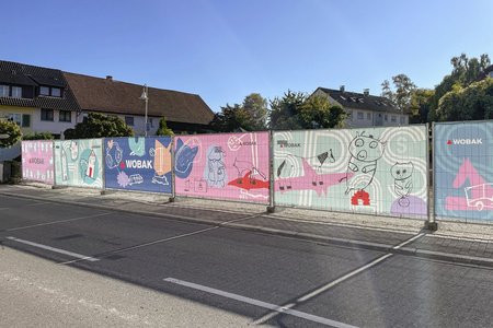 Von Kindern gestaltete Gemälde auf dem Bauzaun, die zeigen, was wichtig für das Zuhause der Kinder ist